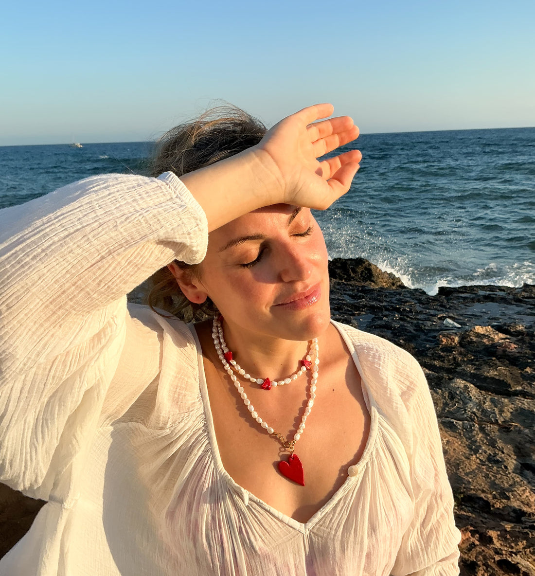 Mujer en la playa luciendo collares de perlas y pieza de cerámica.